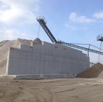 Ein großes Baugerüst transportiert Sand über eine Betonmauer in einer offenen Baustelle unter blauem Himmel.
